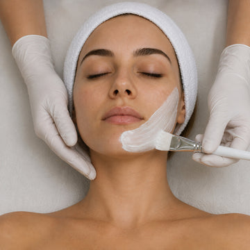 Woman receiving a facial treatment with a brush applying cream to her face.